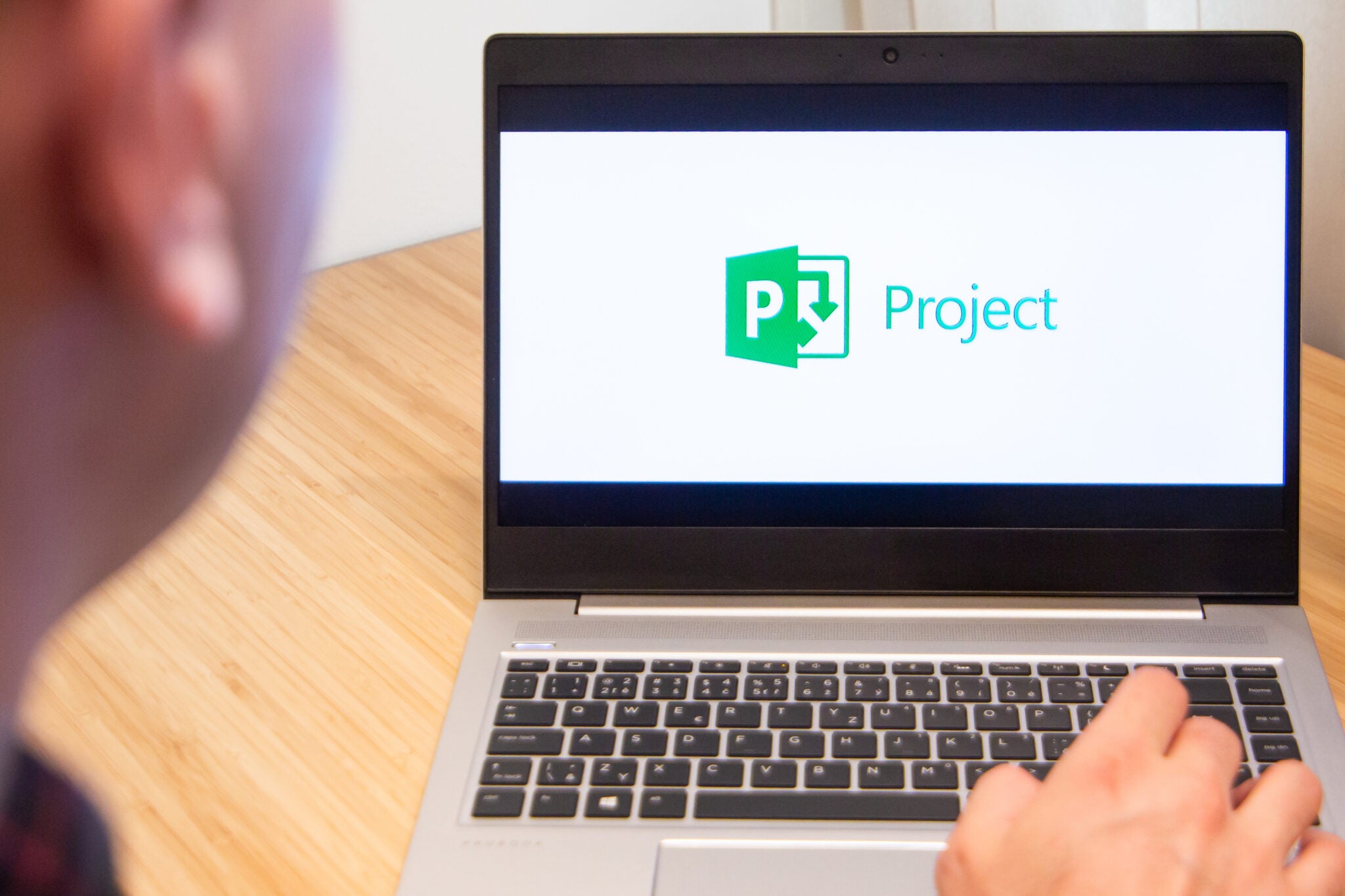 Project manager uses laptop with its screen showing the Microsoft Project logo.
